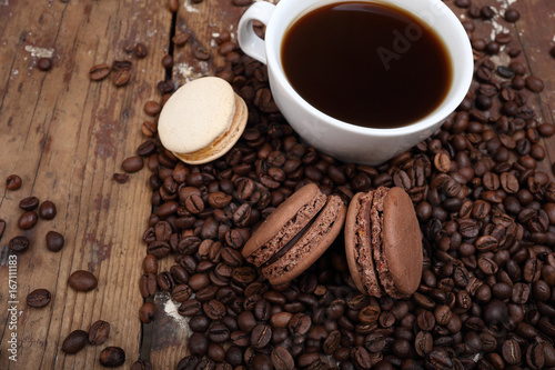 Sweet background of a cup of coffee, coffee beans and cookies macarons on a wooden background. Copyspace on the left.