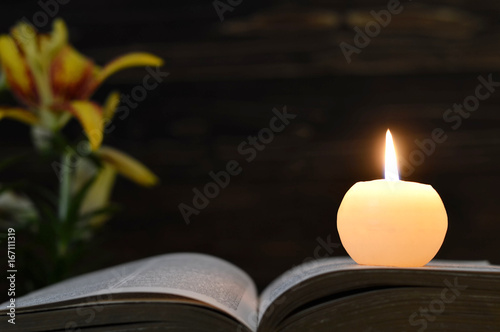 Funeral candle, opened book and flowers on dark wooden background