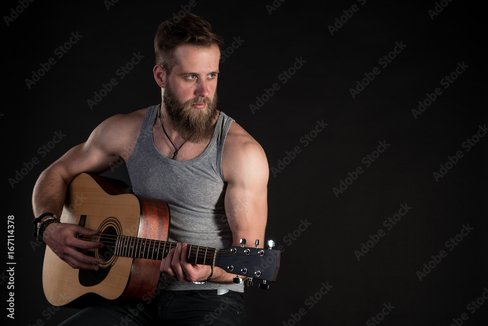 Obraz premium A charismatic man with a beard, playing an acoustic guitar, on a black isolated background. Horizontal frame