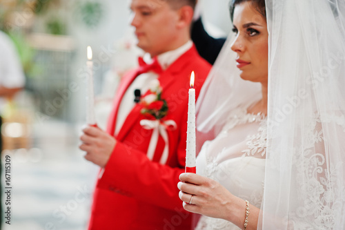 Close-up photo of bride and groom holding candles in the church during wedding ceremony.