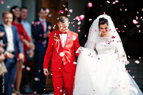 Fabulous wedding couple walking out of the church and people throwing confetti at them.