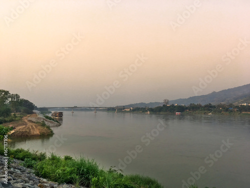 Mekong river and bridge crossing to Laos on evening with sunset and yellow sky. Big river at countryside with mountain and bridge on evening.