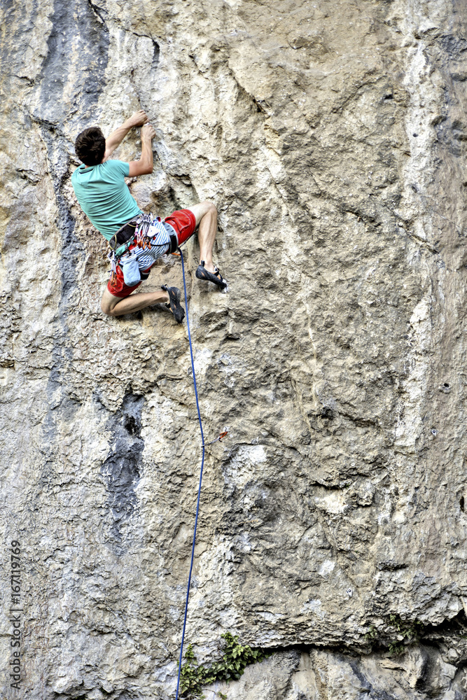 Young man climbing on a limestone wall with wide valley on the background