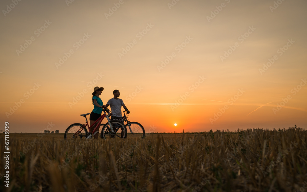 Fototapeta premium Boy and girl with their bicycles watching a dramatic sunset over a rural field