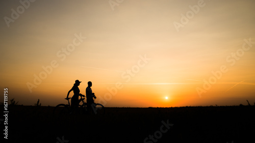 Boy and girl with their bicycles watching a dramatic sunset over a rural field