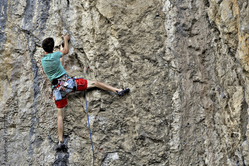 Young man climbing on a limestone wall with wide valley on the background