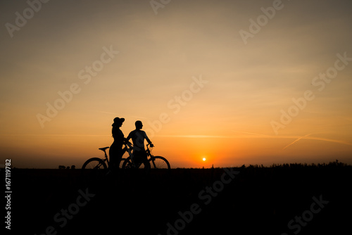 Boy and girl with their bicycles watching a dramatic sunset over a rural field