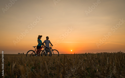 Fototapeta Naklejka Na Ścianę i Meble -  Boy and girl with their bicycles watching a dramatic sunset over a rural field
