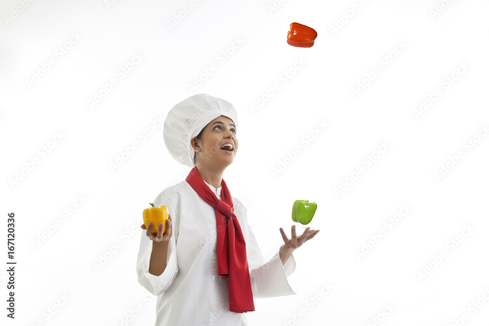 Young female chef juggling bell peppers isolated over white background Young female chef juggling bell peppers isolated over white background