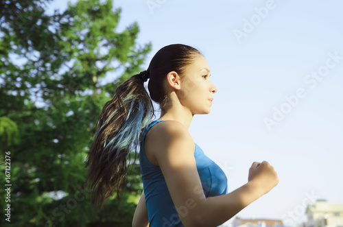 Girl is engaged in fitness in the park, doing exercises. Training on the street in the summer morning. Concept sport healthy lifestyle.