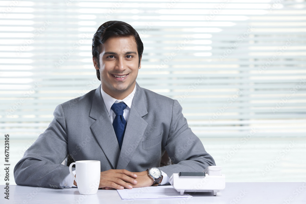 Portrait of smiling businessman sitting at office desk Portrait of smiling businessman sitting at office desk