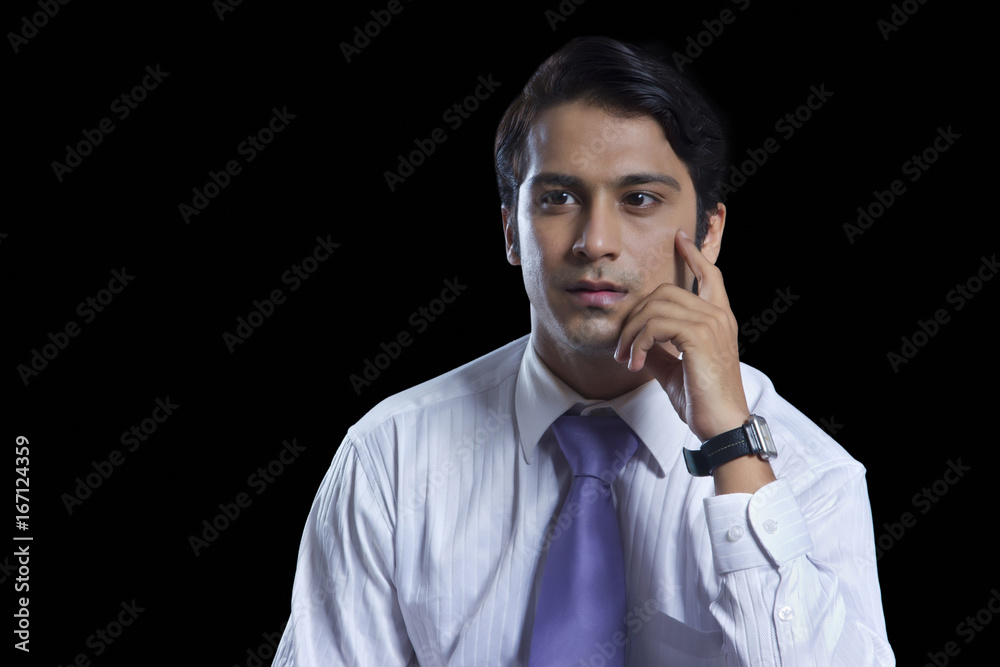 Thoughtful young businessman with hand on chin over black background Thoughtful young businessman with hand on chin over black background
