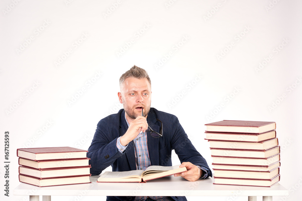 Portrait of middle-aged professor sitting at desk with book heaps on it Portrait of middle-aged professor sitting at desk with book heaps on it