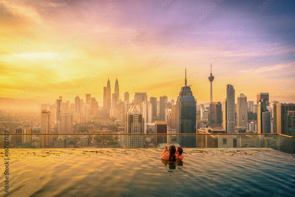 Fototapeta premium Traveler couple woman in swimming pool on the roof top of hotel at sunrise in Kuala Lumpur, Malaysia.
