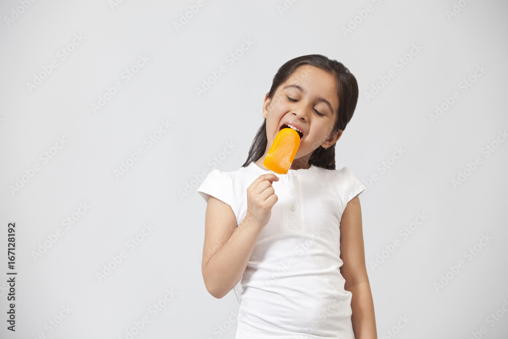 Happy little girl eating ice lolly isolated over gray background Happy little girl eating ice lolly isolated over gray background