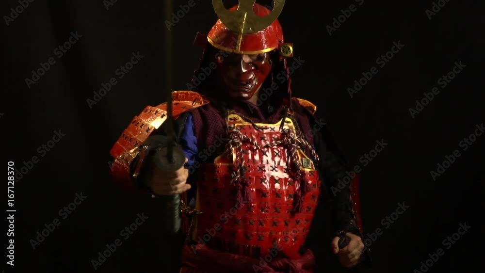A samurai man in red armor and a defensive mask in the form of a demon stands with a katana in his hands, bit slow motion A samurai man in red armor and a defensive mask in the form of a demon stands with a katana in his hands, bit slow motion