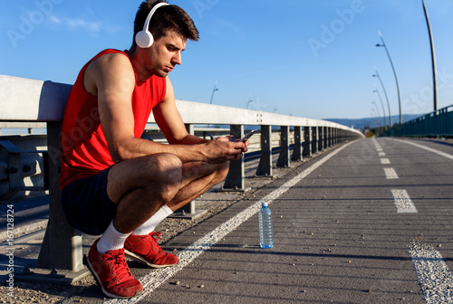 Portrait of young athlete man using mobile phone on bridge.