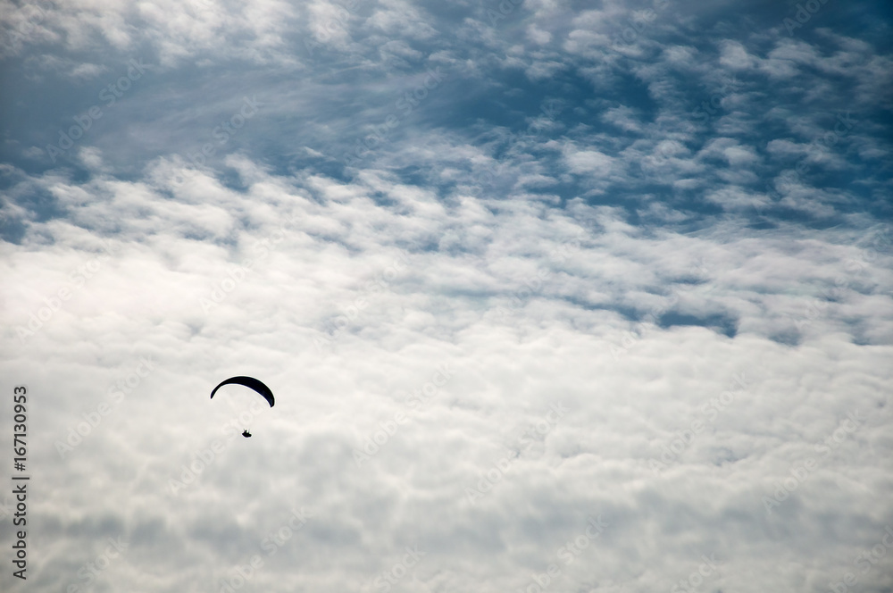 Silhouette of a flying paraglider against a background of clouds in a summer sunny day. Silhouette of a flying paraglider against a background of clouds in a summer sunny day.