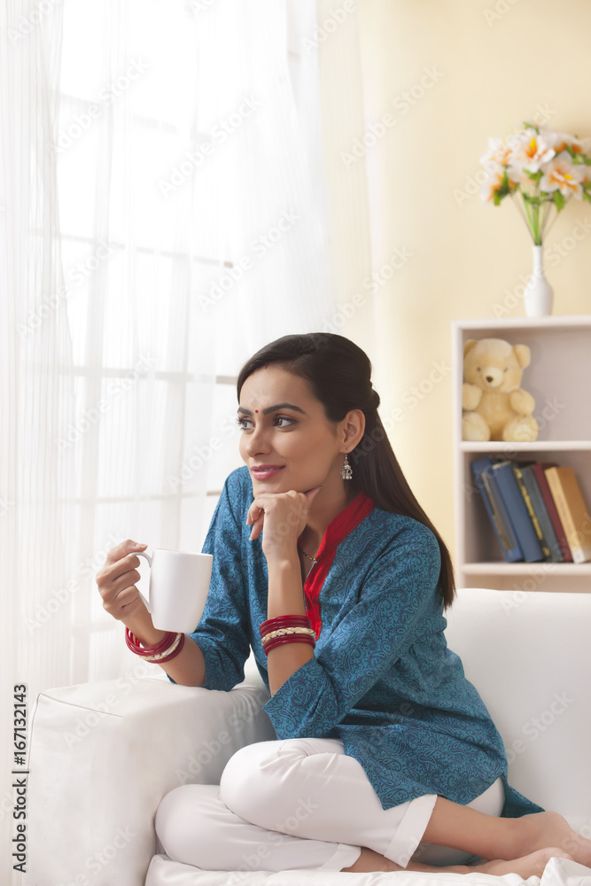 Thoughtful Indian woman having coffee in living room Thoughtful Indian woman having coffee in living room