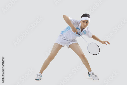 Full length of young woman playing badminton isolated over gray background
