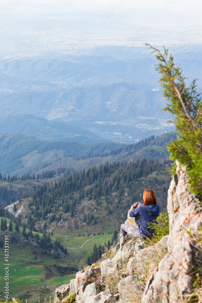 Young woman sitting on top of a mountain. Back view. Tourism concept background.