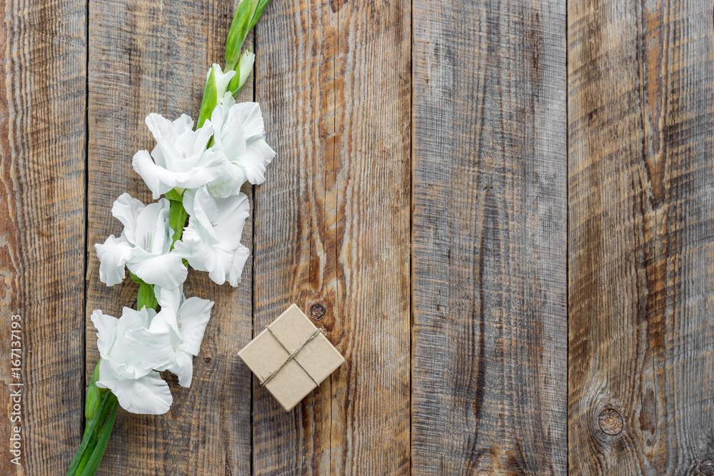 Gift box wrapped in craft paper near flower gladiolus on rustic wooden background top view copyspace Gift box wrapped in craft paper near flower gladiolus on rustic wooden background top view copyspace