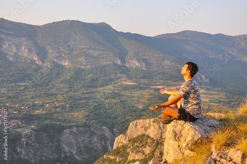 Young man sits on a cliff edge on the top of mountain and meditate. Dangerous Place. Adrenaline. Hiker on the top