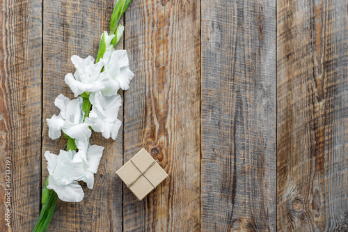 Gift box wrapped in craft paper near flower gladiolus on rustic wooden background top view copyspace