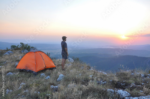 Man watch the sunset end enjoy next to a tent. Hiker camping on top of the mountain.