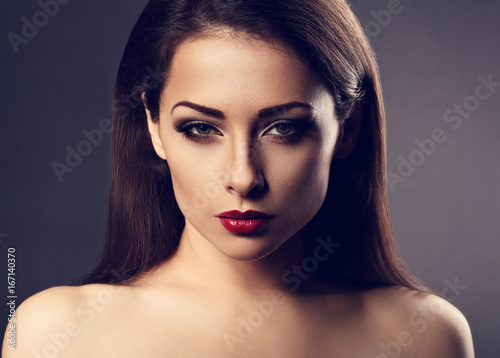 Beautiful vamp makeup sexy woman with hot red lipstick and long eye lashes looking expression on grey background in dramatic light. Closeup toned portrait
