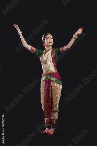 Full length of dancer with arms raised performing Bharatanatyam against black background