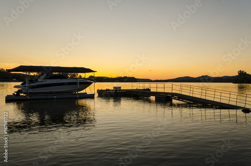 sunset, river view in summer. Colorful landscape summer sunset on the river bank. Sun rays and reflections on water. boat in pier © pellephoto