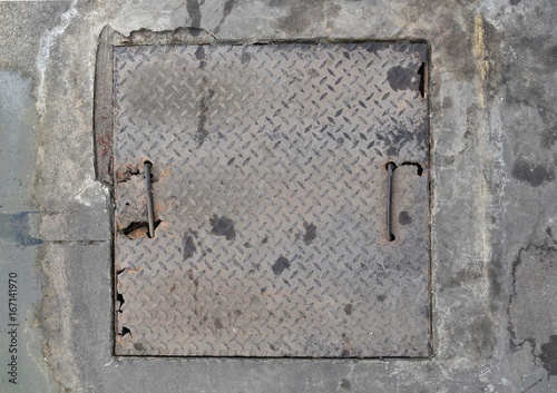 dirty old square metal cover on dirty old concrete