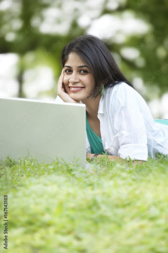 Portrait of young woman using laptop while lying on grass Portrait of young woman using laptop while lying on grass