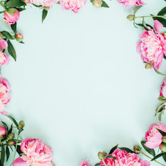 Frame wreath of pink peony flowers, branches, leaves and petals with space for text on blue background. Flat lay, top view. Peony flower texture.