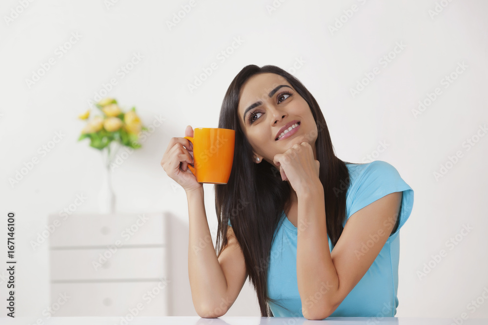 Thoughtful young woman holding coffee cup at home Thoughtful young woman holding coffee cup at home