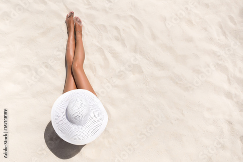 Summer holiday fashion concept - tanning woman wearing sun hat at the beach on a white sand shot from above photo
