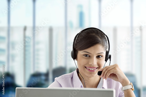 Smiling businesswoman wearing headset and using laptop in office 