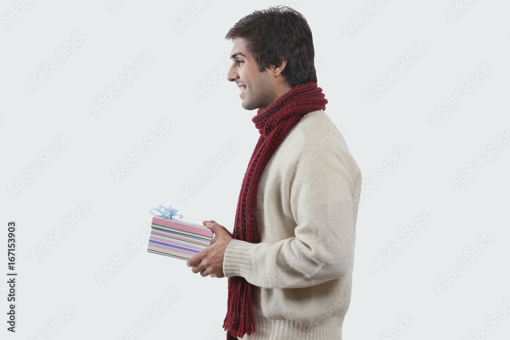 Smiling young man holding gift box over colored background Smiling young man holding gift box over colored background