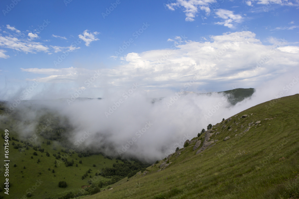Горный пейзаж, туман в горном ущелье, белые облака над склонами, дикая природа
