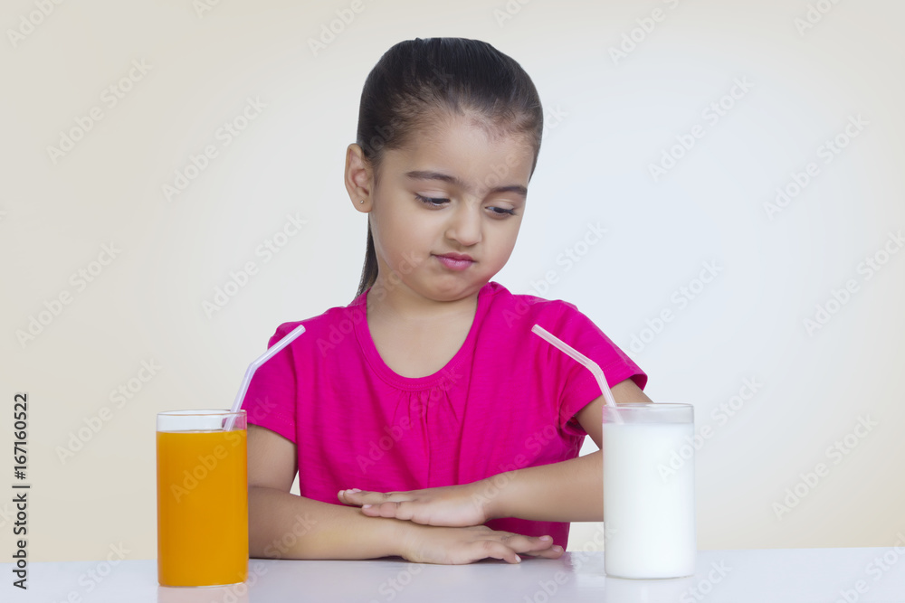 Confused girl choosing between orange juice and milk against colored background Confused girl choosing between orange juice and milk against colored background