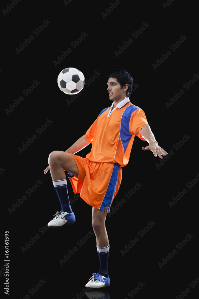 Male soccer player doing kick ups isolated over black background
