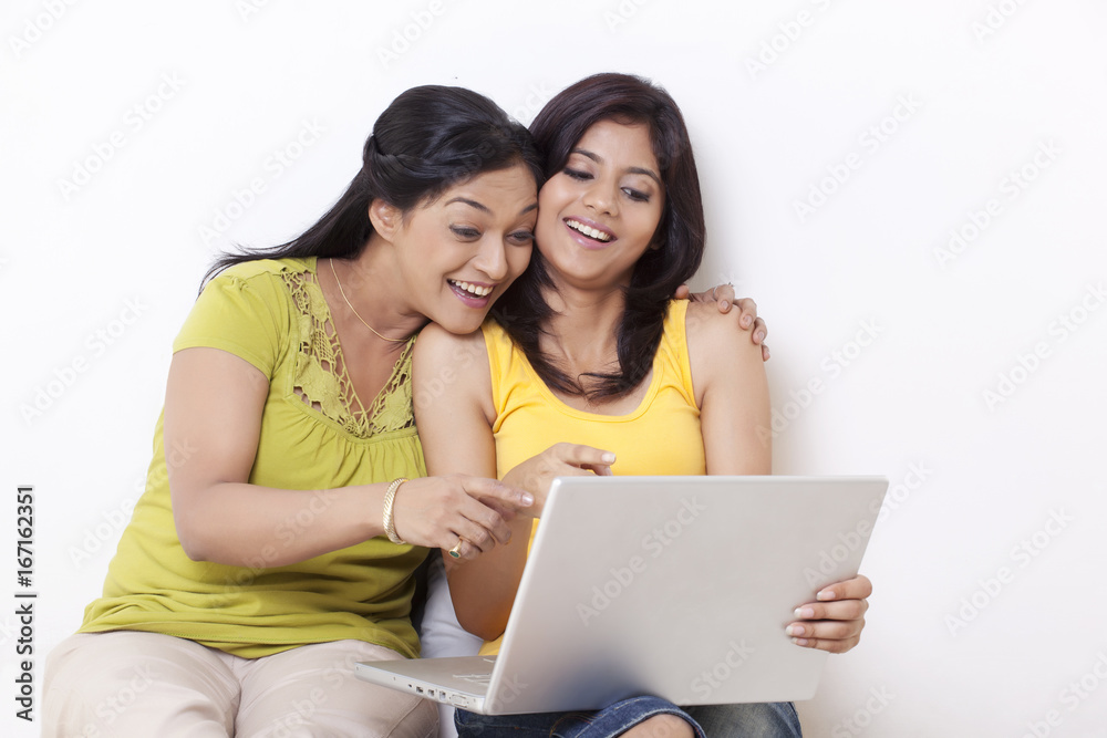 Happy mother and daughter pointing at laptop over white background Happy mother and daughter pointing at laptop over white background