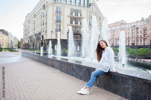 Young and beautiful girl sitting at the fountain and smiling in a new residential complex