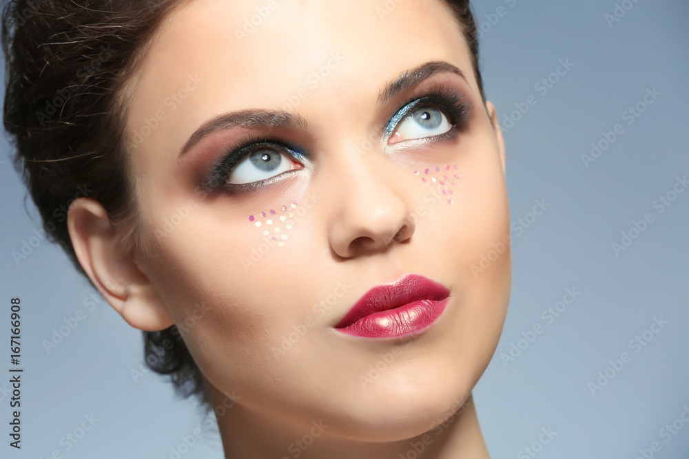 Fototapeta premium Young woman with creative makeup and glitter looking upward, beauty and fashion concept, skincare and cosmetics