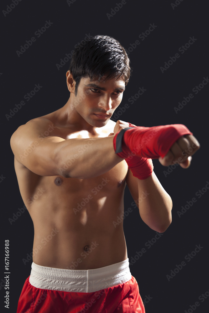 Young male boxer punching isolated over black background