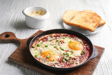 Frying pan with eggs in purgatory on wooden board