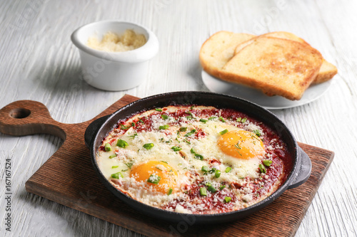 Frying pan with eggs in purgatory on wooden board