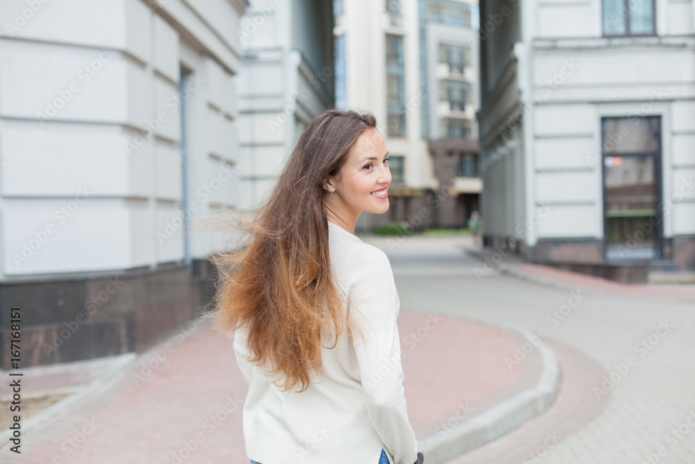 A young and attractive girl with long brown hair in a light sweater riding a scooter in a new residential complex A young and attractive girl with long brown hair in a light sweater riding a scooter in a new residential complex