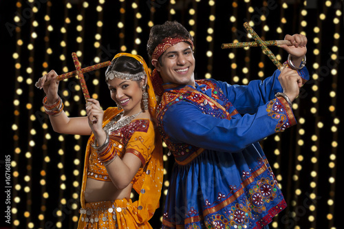 Portrait of happy Indian couple performing Dandiya Raas against neon lights